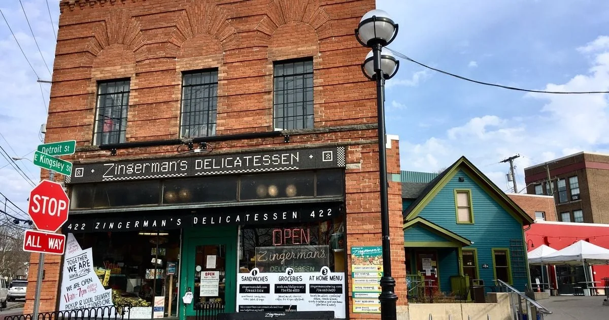 Local Brand Storytelling Frameworks That Actually Work image Exterior photo of Zingerman’s Delicatessen in Ann Arbor, a brick corner storefront with a ‘Zingerman’s Delicatessen’ sign, street signs (Detroit St and E Kingsley St), a stop sign, and an ‘OPEN’ window sign.