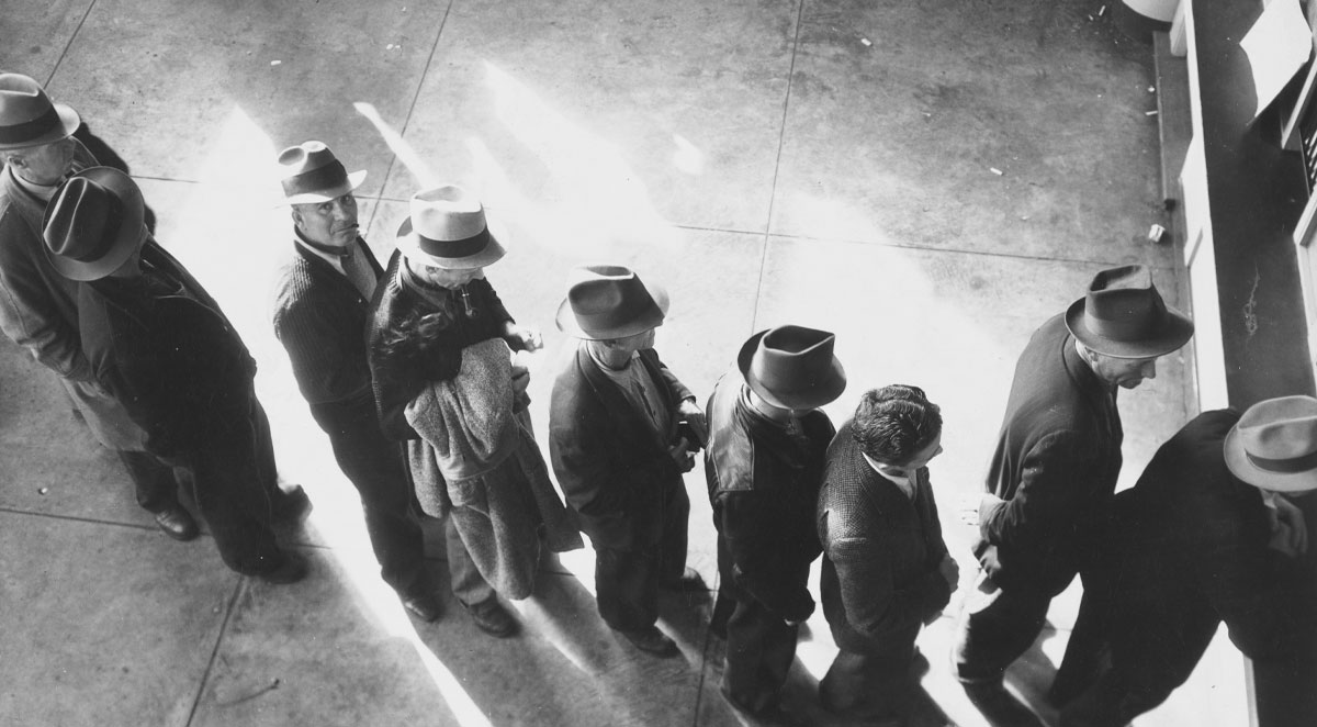 23 of the Best Ways to Recession-Proof Your Small Business image (still image) Unemployment benefits aid begins. Line of men inside a division office of the State Employment Service office at San Francisco, California, waiting to register for benefits on one of the first days the office was open, (1938)